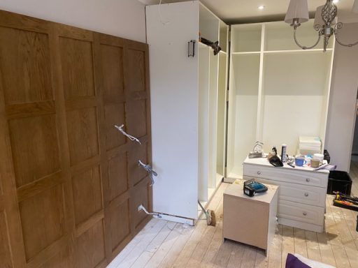 A room with wooden wall panelling, a closet, a bedside table, and scattered items.